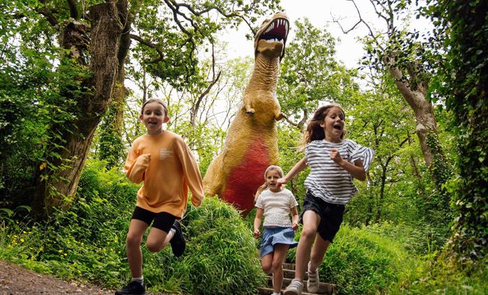 Three girls running away from a huge T-Rex statue on the Dinosaur Trail